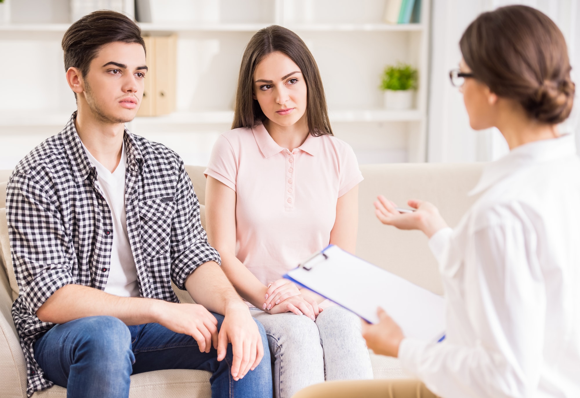 Does Marriage Counseling Work? The image depicts a young couple in a marriage counseling session. The male participant, dressed in a plaid shirt and jeans, appears somewhat concerned or skeptical, sitting with his arms and legs crossed.