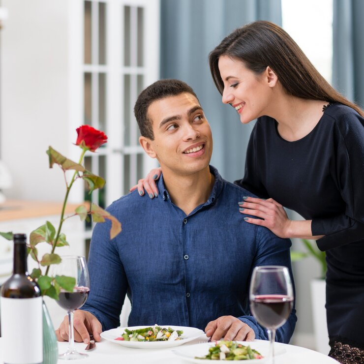 A couple enjoying a romantic Valentine's Day dinner with a rose and wine.